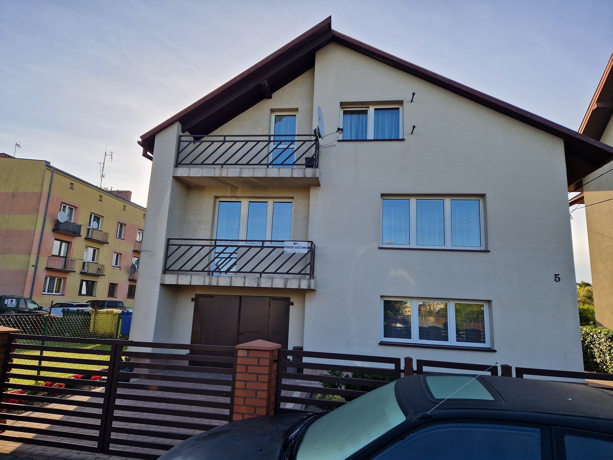 Beżowy domek jednorodzinny przy Mickiewicza 5 w Łasku, balkony z metalowymi balustradami i biały płot